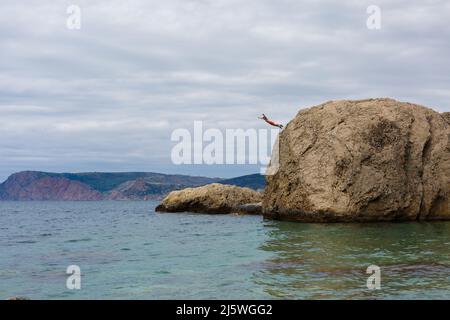 Brave Man salta da High Cliff Rock in acqua di mare Foto Stock