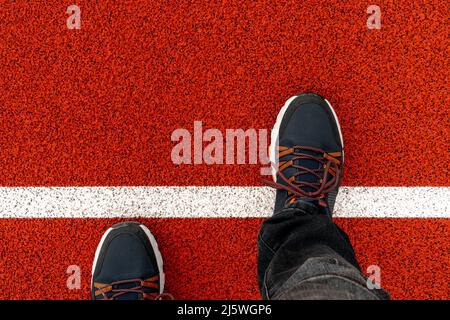 I piedi da uomo in sneakers nere si levano in pista, un piede ha fatto un passo su una linea bianca.camminando attraverso la linea di partenza che rappresenta l'inizio di affari e di vita Foto Stock