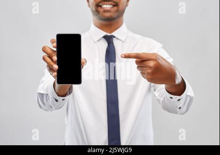 un uomo d'affari indiano sorridente che mostra lo smartphone Foto Stock
