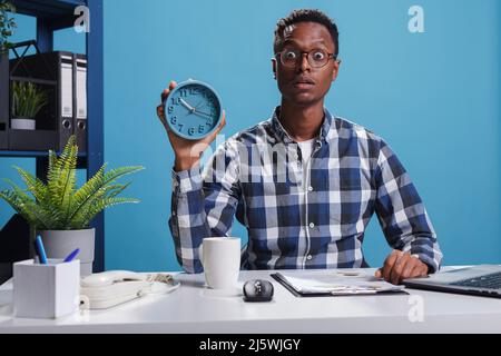 Il leader del team ha scioccato il collega per essere di nuovo in ritardo mentre si mostra ora su orologio. L'uomo d'affari dell'agenzia con faccia di espressione dello shock ha sveglia mentre usando il laptop di lavoro. Foto Stock