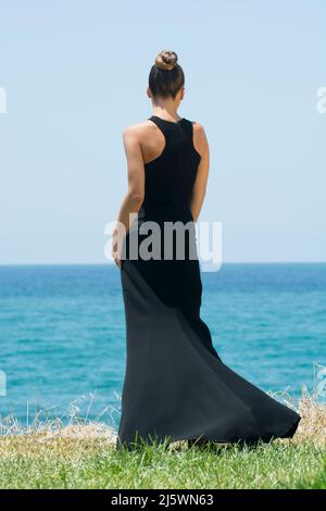 Vista posteriore della giovane donna vestito nero in piedi sulla spiaggia Foto Stock