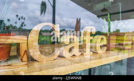 cartello in mockup di legno per il caffè dietro una grande finestra di vetro che riflette la vista all'esterno della caffetteria per sfondo Foto Stock