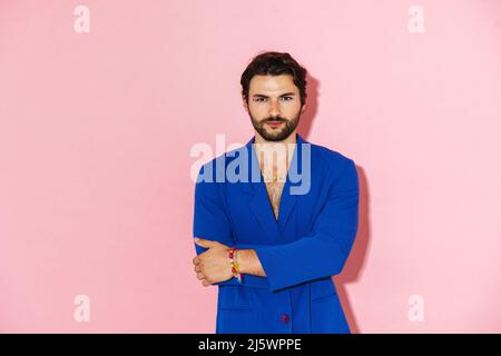 Giovane uomo che indossa una giacca blu che posa e guarda la fotocamera isolata su sfondo rosa Foto Stock