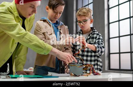 Ragazzi con insegnante che lavorano insieme al progetto con giocattoli elettrici e robot in classe robotica Foto Stock