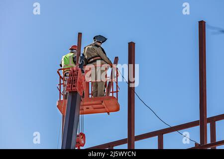 I costruttori maschi lavorano in altezza in una culla di sollevamento, creando la struttura in ferro dell'edificio Foto Stock