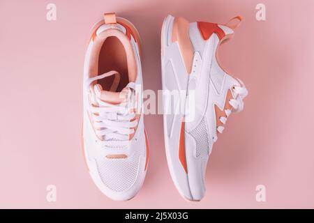 Sneaker bianche da donna con inserti in corallo su sfondo rosa. Vista dall'alto. Disposizione piatta. Foto Stock