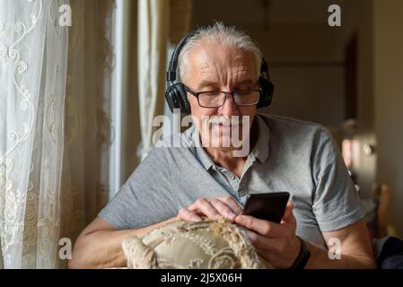 Uomo anziano in cuffie che ascolta la musica dal telefono cellulare Foto Stock