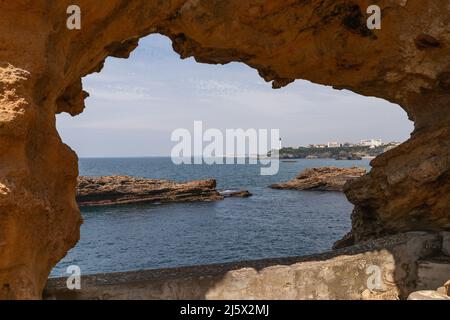 Vista della costa di Biarritz e del faro attraverso la finestra bagnata in pietra dal mare per millenni. Pyrenees-Atlantiques dipartimento, Paesi Baschi francesi Foto Stock