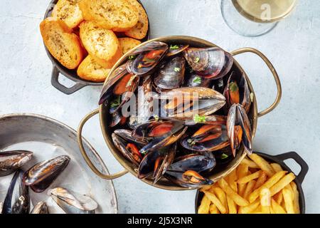 Cozze belghe con patatine fritte e pane tostato, sparate dall'alto su un fondo di ardesia Foto Stock