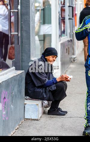 Una povera vecchia donna vestita di nero e un copricapo siede in una porta di negozio implorando la strada a Bucarest, capitale della Romania, Europa centrale Foto Stock