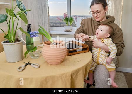 Madre e divertente lavoro del bambino con le piante nel giardino domestico. La mamma insegna al bambino come prendersi cura dei fiori Foto Stock