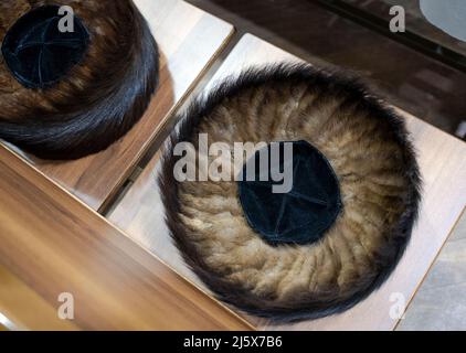 Un cappello di pelliccia di shtreimel indossato da alcuni ebrei ortodossi durante il Sabbath & le feste religiose. Su una panchina in una sinagoga a Brooklyn, New York City. Foto Stock