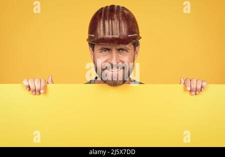 felice uomo maturo costruttore in casco dietro carta gialla per copia spazio, felice giorno del lavoro Foto Stock