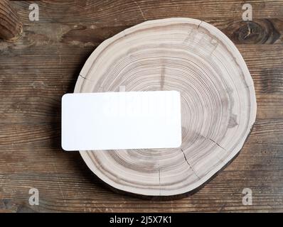 Cartoncino di carta vuoto rettangolare su fetta di legno a croce su vecchio tavolo rustico in legno resistente agli agenti atmosferici. Mock up. Spazio di copia. Vista dall'alto. Orientamento orizzontale. Foto Stock