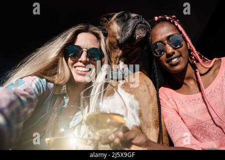 Giovani amici multirazziali e cane da compagnia che festeggia con il vino mentre fanno un selfie - Focus on Right Girl Foto Stock