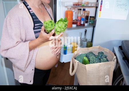 Donna incinta che mette via i generi alimentari sani in cucina Foto Stock