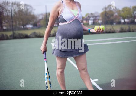 Donna incinta in vestito giocando a tennis sul campo da tennis Foto Stock