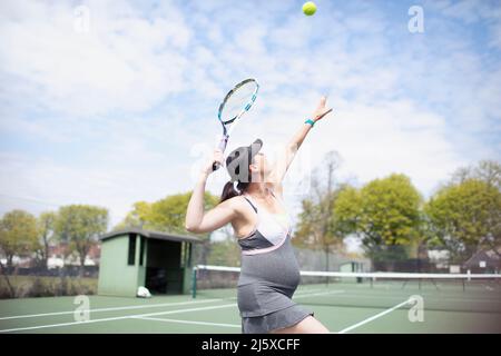 Donna incinta che gioca a tennis sul campo da tennis soleggiato Foto Stock