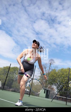 Donna incinta che gioca a tennis sul campo da tennis soleggiato Foto Stock