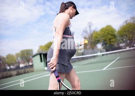 Donna incinta che gioca a tennis sul campo da tennis soleggiato Foto Stock