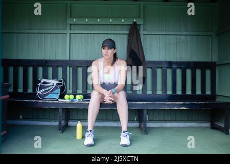 Donna incinta che riposa su panchina al campo da tennis Foto Stock