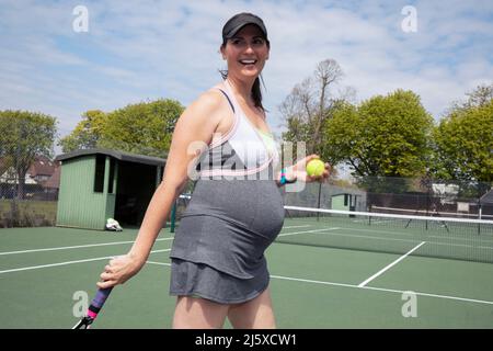 Donna incinta felice che gioca a tennis sul campo da tennis soleggiato Foto Stock