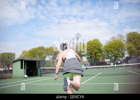 Donna che gioca a tennis su un campo da tennis soleggiato Foto Stock