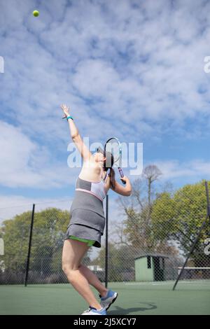 Donna incinta che gioca a tennis sul campo da tennis soleggiato Foto Stock