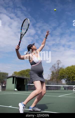 Donna incinta che serve pallina da tennis sul campo da tennis soleggiato Foto Stock