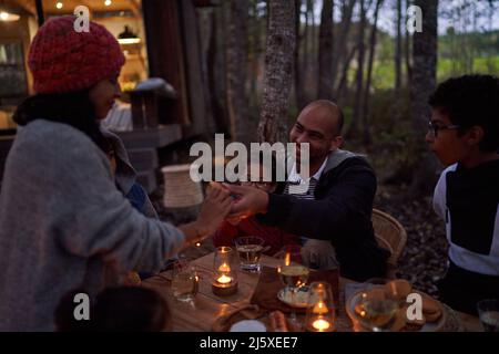 Famiglia che mangia al tavolo a lume di candela fuori cabina Foto Stock