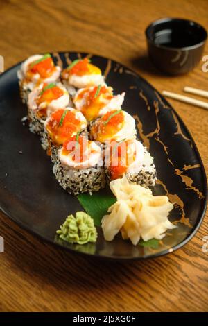 Una serie di sushi roll con salmone, caviale, avocado e sesamo nero in primo piano. Fuoco selettivo Foto Stock