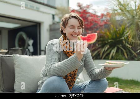 Felice giovane donna che mangia cocomero sul patio estivo Foto Stock
