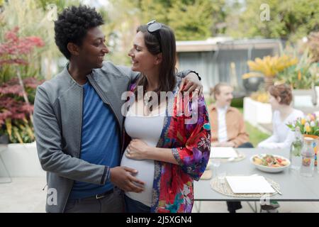 Felice coppia incinta abbraccio sul patio Foto Stock