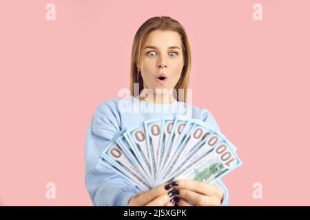 Stupito giovane donna con la bocca larga aperta e gli occhi guardando bollette dollaro tenuta in mani. Foto Stock