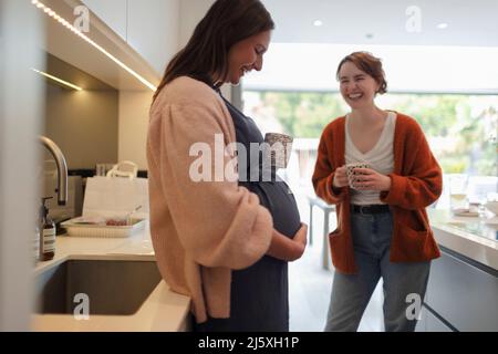 Donna incinta felice con un amico in cucina Foto Stock