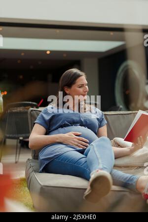 Donna incinta libro di lettura sulla sedia lounge patio Foto Stock