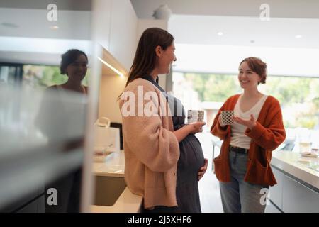 Donna incinta che parla con l'amico e beve il tè in cucina Foto Stock