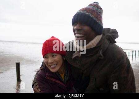 Felice coppia affettuosa in caldo abbigliamento abbracciato sulla spiaggia invernale Foto Stock