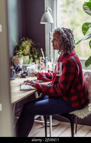 Donna anziana che lavora alla scrivania in ufficio a casa Foto Stock