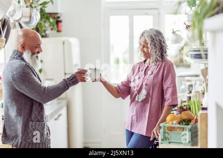 Una coppia di persone anziane che tostano le tazze di caffè in cucina Foto Stock