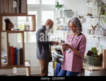 Donna anziana che usa lo smartphone in cucina Foto Stock