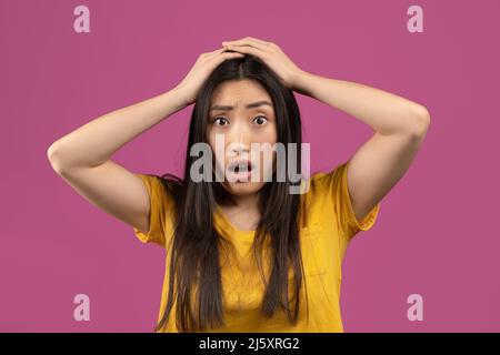 Notizie incredibili. Scioccata donna asiatica toccando la sua testa, non può credere sorprendente offerta o vendita, sfondo viola Foto Stock