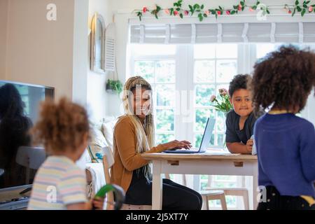 Felice madre che lavora da casa e guarda i bambini giocare Foto Stock