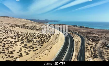 Vista dall'alto di una strada tortuosa attraverso le dune sabbiose delle isole di Fuerteventura. Foto Stock