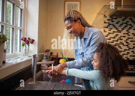 Felice madre e figlia lavarsi le mani al lavandino della cucina Foto Stock