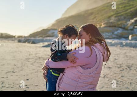 Madre affettuosa che tiene il figlio con la sindrome di Down sulla spiaggia soleggiata Foto Stock