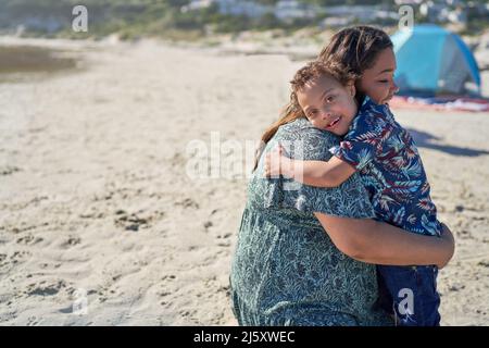 Ritratto ragazzo felice con sindrome di Down che abbraccia la madre sulla spiaggia Foto Stock