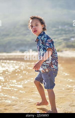 Ritratto ragazzo con sindrome di Down che guado in oceano sulla spiaggia soleggiata Foto Stock