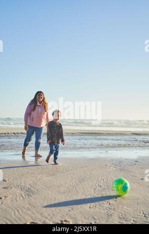 Madre e figlio giocano con la palla di calcio sulla spiaggia soleggiata Foto Stock