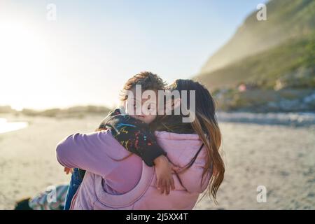 Madre che tiene il figlio con la sindrome di Down sulla spiaggia soleggiata Foto Stock